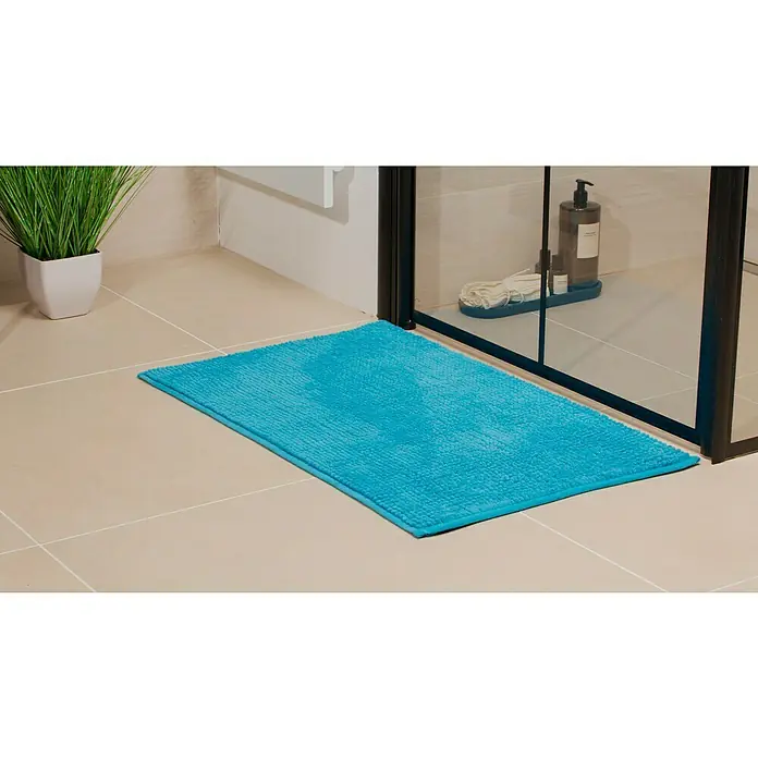 Camargue Badteppich Zottel - 50 x 80 cm, Türkis, 100% Polyester - Ein blauer Badteppich liegt vor einer Duschkabine auf hellen Fliesen, neben einer grünen Pflanze. Der Teppich sorgt für Komfort und Farbe im Badezimmer.