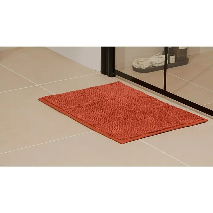 Badteppich Bubble - 40 x 60 cm, Rot, 100% Polyester - Ein rechteckiger, orangefarbener Badteppich liegt auf hellen Fliesen vor einer Duschkabine. Der Teppich hat eine strukturierte Oberfläche.