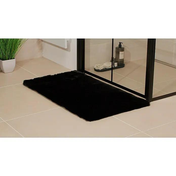 Badteppich Happy - 50 x 90 cm, Schwarz, 100% Polyester - Ein schwarzer, flauschiger Teppich liegt vor einer modernen Dusche auf hellen Fliesen und sorgt für Komfort und Stil im Badezimmer.