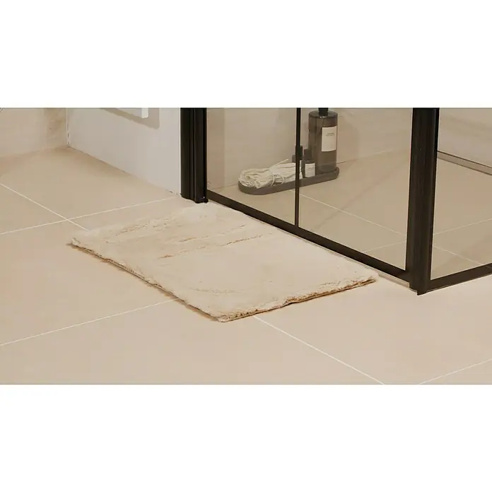 Badteppich Happy - 40 x 60 cm, Beige, 100% Polyester - Ein rechteckiger, beiger Badteppich liegt vor einer dunklen Duschkabine auf hellen Fliesen.