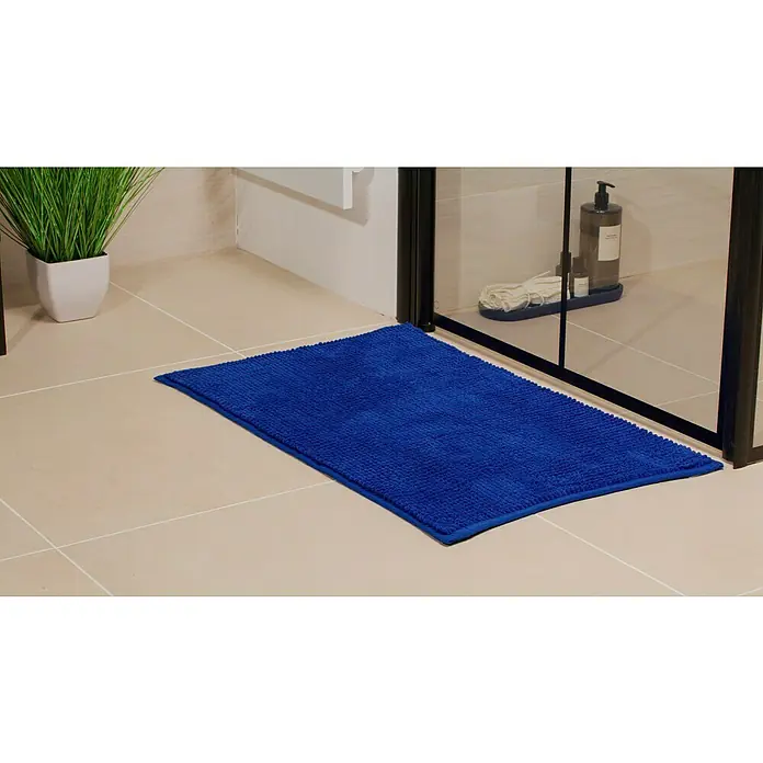 Camargue Badteppich Zottel - 50 x 80 cm, Dunkelblau, 100% Polyester - Blauer Badteppich vor einer Dusche auf beigem Fliesenboden. Im Hintergrund eine Pflanze und Badutensilien.