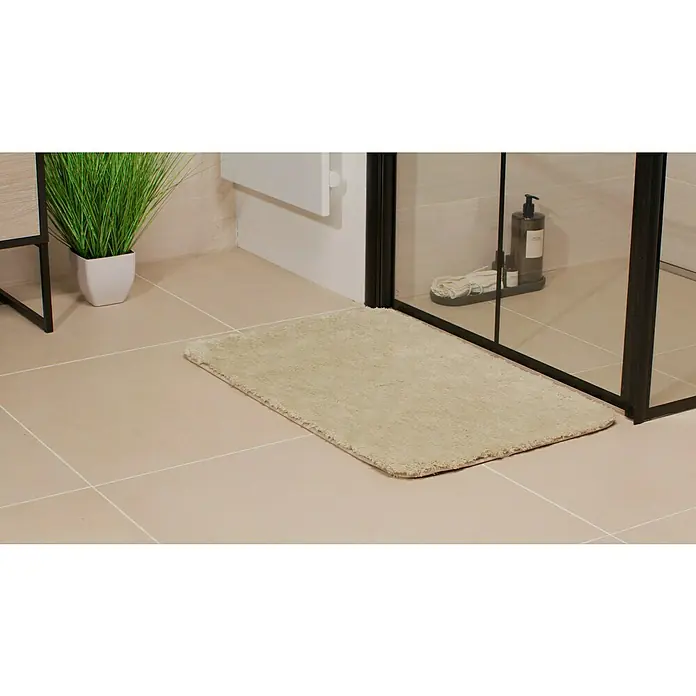 Camargue Badteppich Wuschel - 80 x 50 cm, Beige - Ein rechteckiger, beiger Badteppich liegt vor einer Duschkabine in einem Badezimmer mit beigen Fliesen.