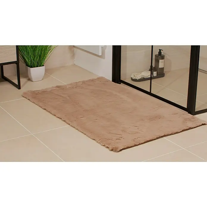 Badteppich Happy67 x 110 cm, Taupe, 100% Polyester - Ein beiger, rechteckiger Teppich mit Fransen liegt im Badezimmer vor einer begehbaren Dusche und einer Pflanze.