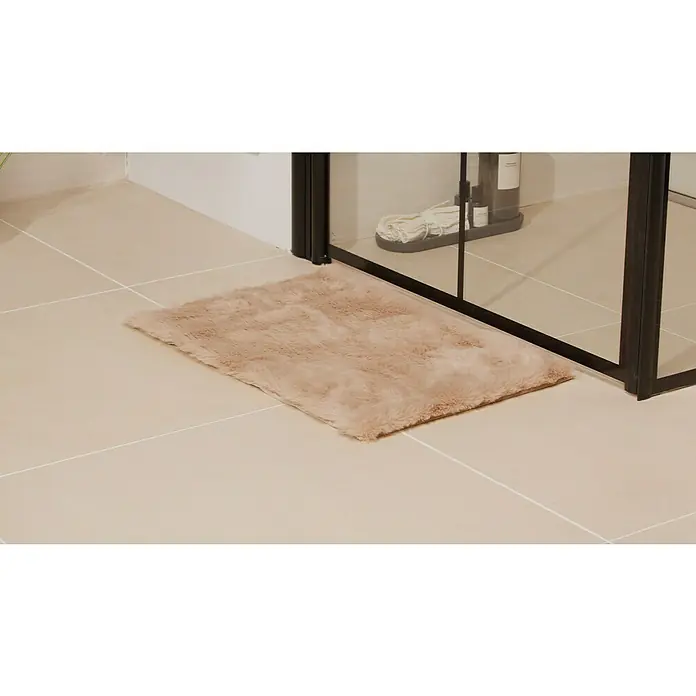 Badteppich Happy - 40 x 60 cm, Taupe, 100% Polyester - Ein weicher, beigefarbener Badteppich liegt vor einer Duschkabine auf hellen Fliesen und sorgt für Komfort und Wärme im Badezimmer.