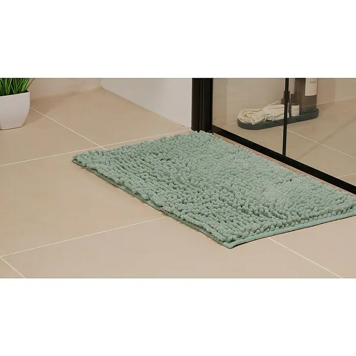 Badteppich Bubble - 45 x 75 cm, Celadon, 100% Polyester - Ein mintgrüner, rechteckiger Badteppich mit Noppen liegt auf beigen Fliesen vor einer Duschkabine. Dekorative und funktionale Ergänzung für jedes Badezimmer.