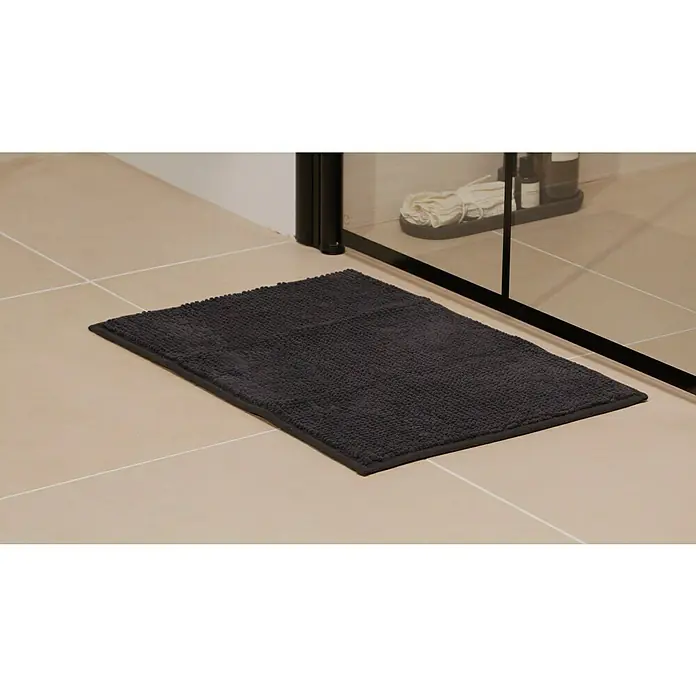 Badteppich Bubble - 40 x 60 cm, Schwarz, 100% Polyester - Ein dunkelgrauer Badezimmerteppich liegt auf hellen Fliesen vor einer Duschkabine, der Komfort und Stil in Ihr Badezimmer bringt.