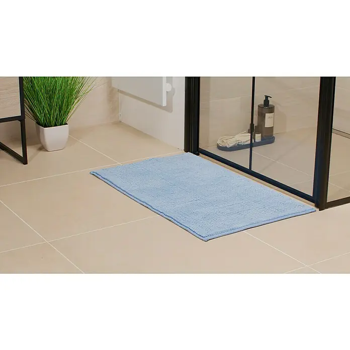 Camargue Badteppich Zottel - 50 x 80 cm, Blau, 100% Polyester - Ein hellblauer Badteppich liegt vor einer Duschkabine auf beigen Bodenfliesen und sorgt für einen Farbtupfer im Badezimmer.
