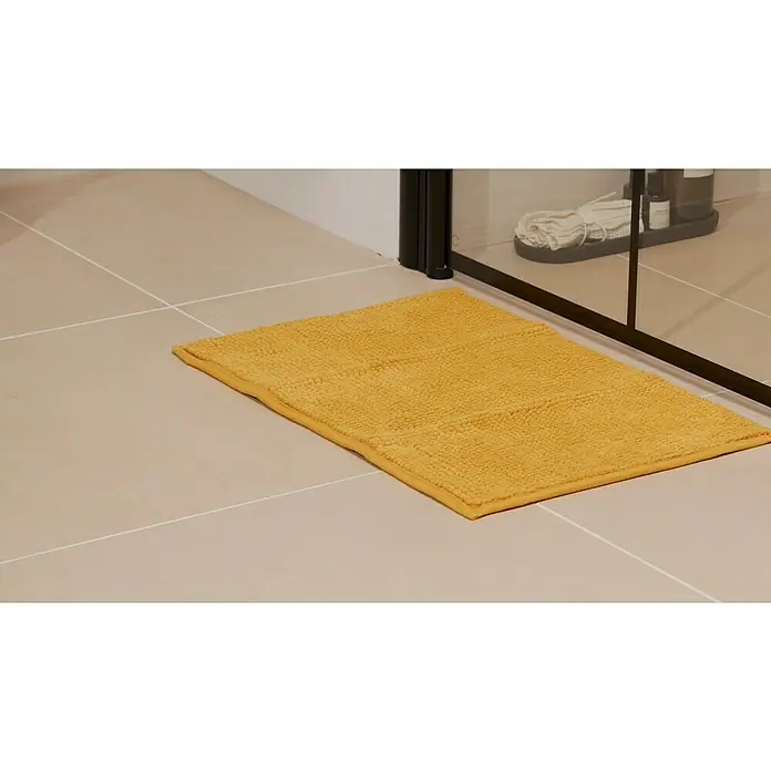 Badteppich Bubble - 40 x 60 cm, Gelb, 100% Polyester - Das Foto zeigt eine rechteckige, senfgelbe Badematte aus Baumwolle mit Fransen auf hellbeige Fliesen in einem Badezimmer.