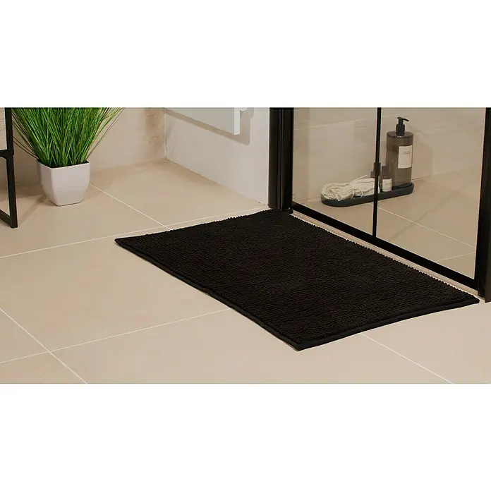 Camargue Badteppich Zottel - 50 x 80 cm, Schwarz, 100% Polyester - Ein rechteckiger, schwarzer Badezimmerteppich liegt auf hellen Fliesen vor einer Duschkabine. Er bietet Komfort und Stil im Badezimmer.