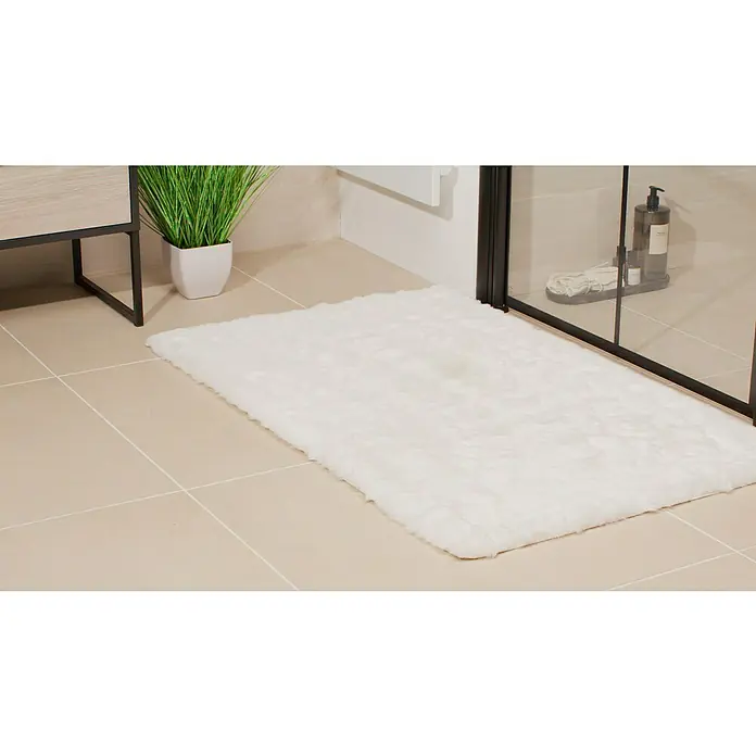 Badteppich Happy - 67 x 110 cm, Weiß, 100% Polyester - Ein rechteckiger, flauschiger, weißer Badteppich liegt auf einem hellbraunen Fliesenboden in einem Badezimmer.