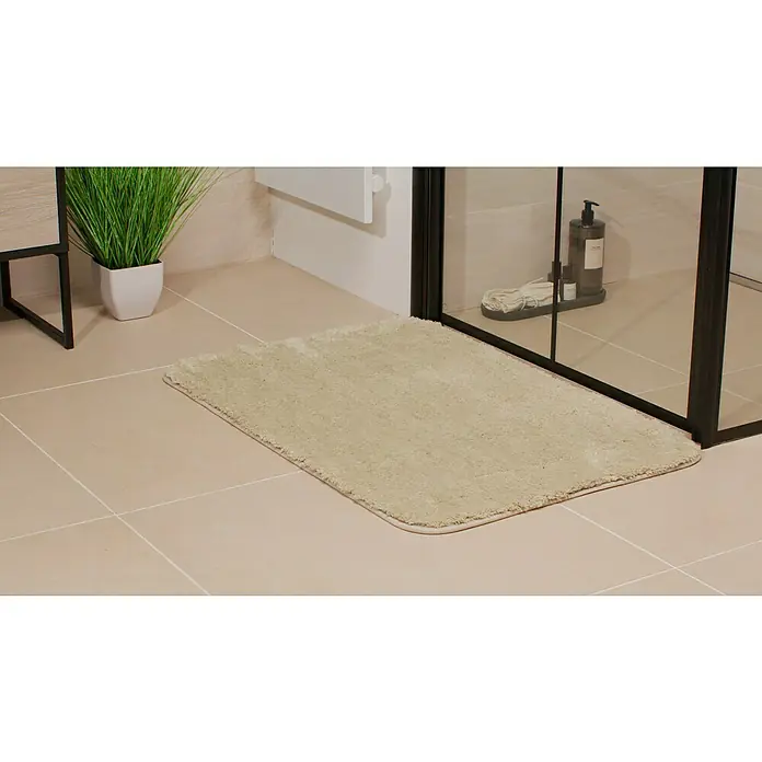 Camargue Badteppich Wuschel - 90 x 60 cm, Beige - Ein beiger Badteppich liegt auf dem Badezimmerboden, neben einer Dusche und einem Waschbecken mit Pflanze, für ein gemütliches Ambiente.