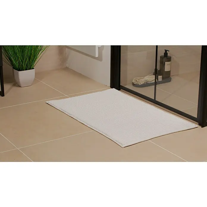 Camargue Badteppich Zottel - 50 x 80 cm, Weiß, 100% Polyester - Eine rechteckige, weiße Badematte liegt vor einer Duschkabine auf beigen Fliesen und bietet Komfort und Sicherheit nach dem Duschen.