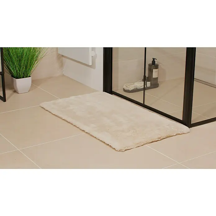 Badteppich Happy - 50 x 90 cm, Beige, 100% Polyester - Weicher, rechteckiger Badteppich in Cremefarbe, der auf beigen Fliesen vor einer Duschkabine liegt. Eine stilvolle Ergänzung für jedes Badezimmer.