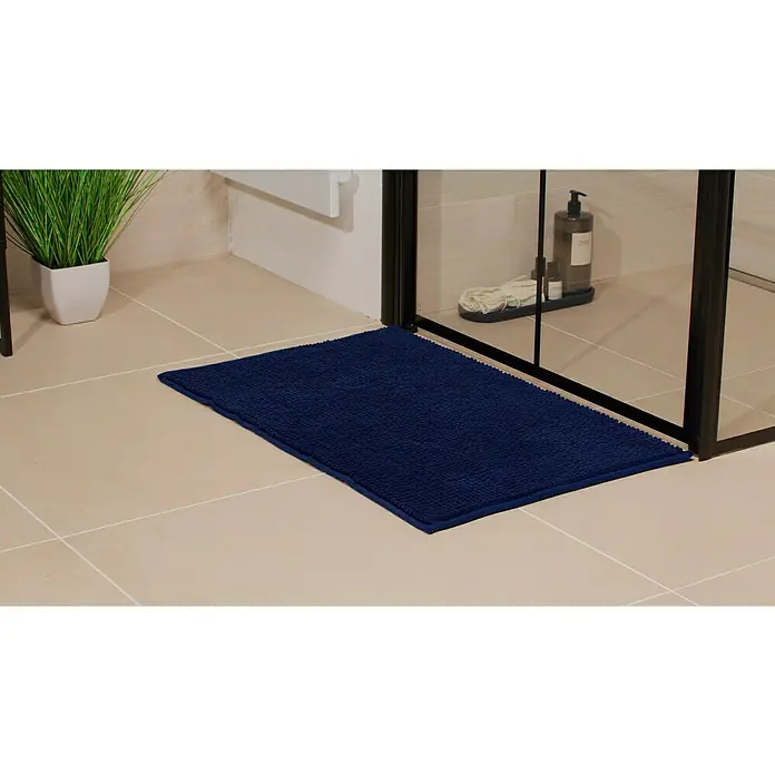 Camargue Badteppich Zottel50 x 80 cm, Marine, 100% Polyester - Ein rechteckiger, marineblauer Badteppich aus saugfähigem Material liegt vor einer Duschkabine, ergänzt durch eine Kunstpflanze und Pflegeprodukte.
