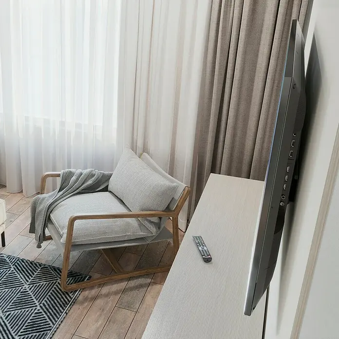 Hama TV-Wandhalterung starr - Passend für: Bildschirmgröße: 94 - 229 cm (37" - 90") bis 100 kg - Ein gemütlicher Sessel mit einem grauen Überwurf neben einem modernen Fernseher auf einer Kommode.