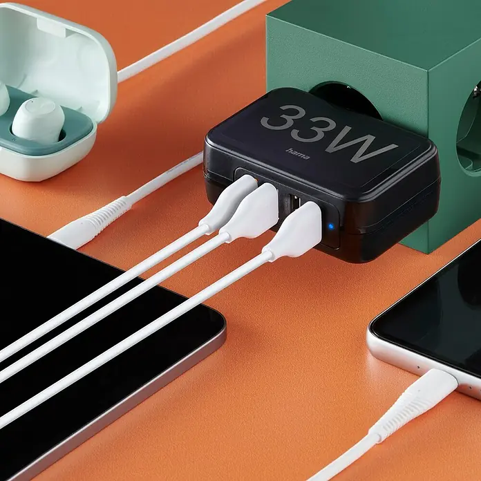Hama USB-Adapter Schnellladegerät 4x USB-A 33W - Schwarz, USB A-Stecker - Nahaufnahme eines Hama 33W Ladegeräts mit mehreren angeschlossenen Geräten und Kabeln auf orangefarbenem Hintergrund.