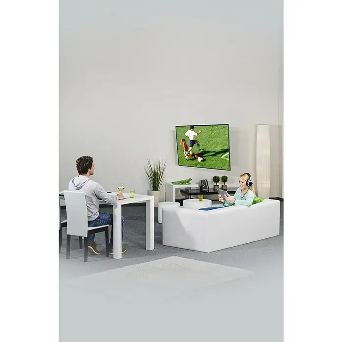 Hama TV-Wandhalterung schwenkbar, neigbar - Passend für: Bildschirmgröße: 81 - 165 cm (32"- 65") bis 20 kg - Wohnzimmer mit weißem Sofa und Fernseher. Die Frau sitzt auf dem Sofa mit einem Tablet, während der Mann am Tisch sitzt und etwas trinkt.