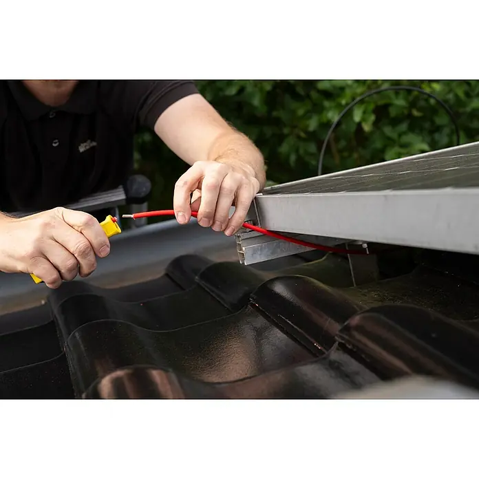 Weicon Kabelentmanteler Mini-Solar - 4 mm² - 6 mm², Gelb - Ein Mann befestigt ein rotes Kabel an einem Solarpanel auf einem Dach, mit einem gelben Abisolierwerkzeug in der Hand für präzise Verbindungen.