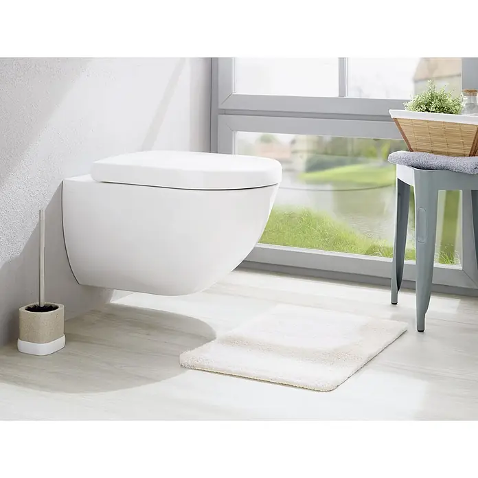 Venus Nara WC-Bürstengarnitur - Polyresin, Beige - Wandhängendes WC in einem modernen Badezimmer mit Fenster und weißem Teppich. Ein WC-Bürstenhalter steht neben der Toilette.