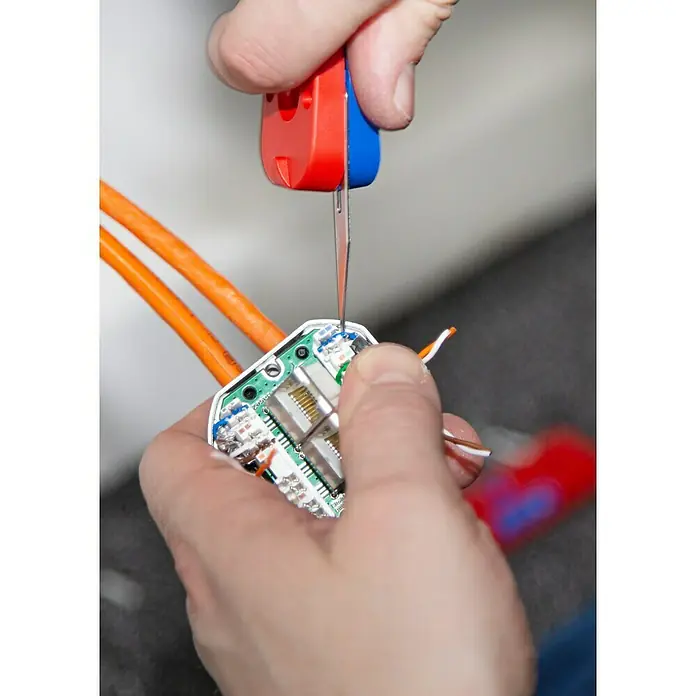 Weicon Anlegewerkzeug LSA Sensor No. 40 - Blau, Rot, Passend für: Beschaltung LSA-Baureihe - Nahaufnahme von Händen, die mit einem Werkzeug eine Netzwerkdose bearbeiten, wobei die Kabel und die Elektronik im Detail zu sehen sind.
