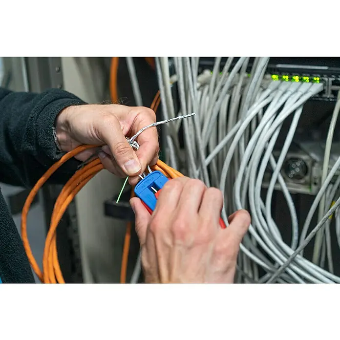 Weicon Kabelentmanteler Präzisions-Abisolierer S - Passend für: Feindrähtige Leiter und Litzen, PVC-, PTFE/Teflon-, Kynar-Isolationen von 0,12 mm - 0,8 mm - Ein Elektriker, der mit einem Abisolierwerkzeug an Kabeln arbeitet. Kabel sind mit einem Netzwerk-Switch verbunden, der an ist.