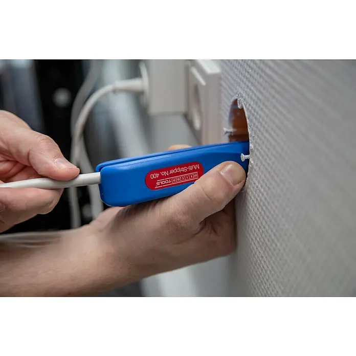 Weicon Kabelentmanteler Multi-Stripper No. 400 - 0,5 mm² - 6 mm², Blau, Rot - Elektriker mit dem Weicon TOOLS Multi-Stripper No. 400 beim Abisolieren eines Kabels an einer Wandsteckdose, Nahaufnahme.