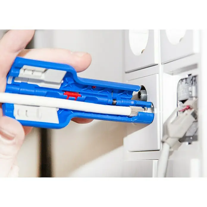 Weicon Kabelentmanteler Coax-Stripper No. 1 F Plus - Blau, Rot, Passend für: Koaxialkabel, bzw. Antennen- und Übertragungskabel - Nahaufnahme eines Koaxialkabel-Abisolierwerkzeugs in Blau, das ein weißes Kabel abisoliert, neben einer weißen Wandsteckdose.
