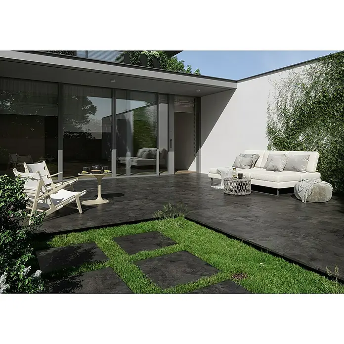 Queens Terrassenfliese - 59,3 x 119,3 x 2 cm, Graphit, Matt - Elegante Terrasse mit dunklen Bodenfliesen, weißen Gartenmöbeln und grünen Akzenten. Die Fliesen schaffen eine moderne und stilvolle Atmosphäre im Außenbereich.