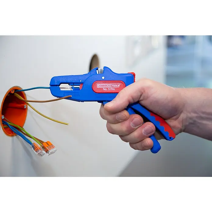 Weicon Kabelentmanteler Abisolierzange No. 5 Pro - 0,2 mm² - 16 mm², Blau, Rot - Abisolierzange Weicon Tools No. 5 Pro beim Abisolieren eines Drahtes vor einer orangefarbenen Anschlussdose an einer Wand.