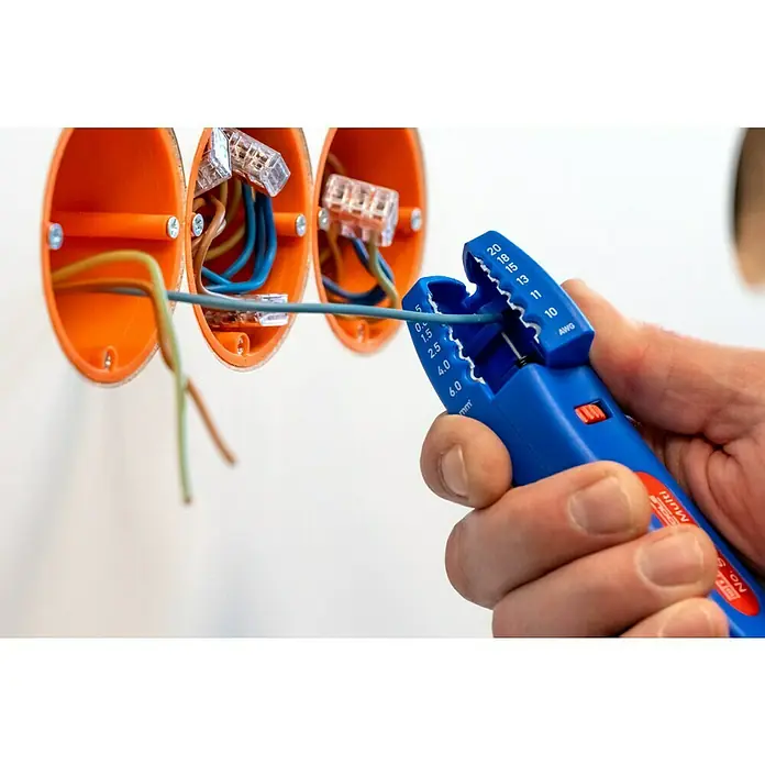 Weicon Kabelmesser No. S 4-28 Multi - 0,5 mm² - 6 mm², Blau, Rot - Ein Elektriker benutzt eine blaue Abisolierzange, um ein graues Kabel vor einer orangefarbenen Verteilerdose zu bearbeiten.