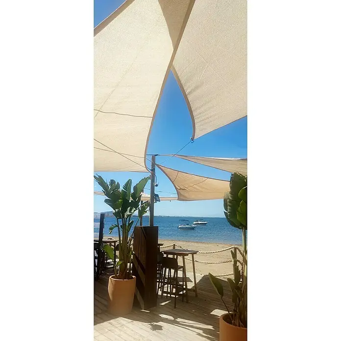 Faura Toldo vela PES - L x An: 3,6 x 3,6 m, Beige, Triangular - Vista desde la elegante cafetería de playa con toldos al mar con barcos, enmarcada por plantas. Ambiente acogedor para horas de relax.