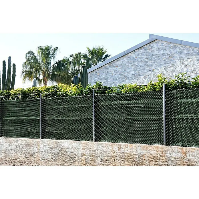 Faura Malla sombreadora - L x Al: 5 x 4 m, Verde, Plástico - Un primer plano de una valla de jardín verde, con una pared de piedra al fondo y una exuberante vegetación encima. Valla de pantalla.