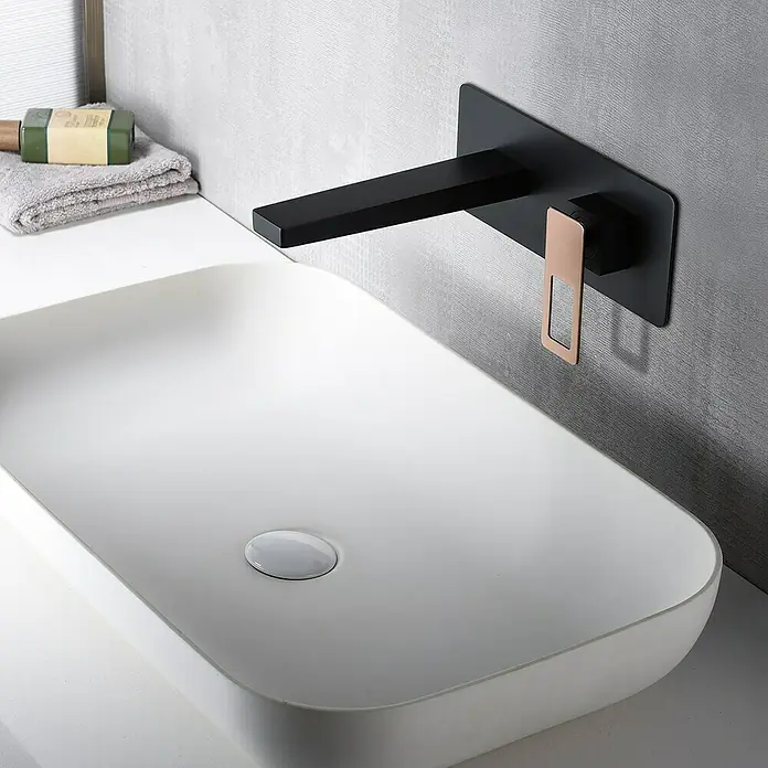 Imex Suecia Grifo de lavabo empotrado - Negro/Oro rosa - Grifo negro de pared con detalles en cobre sobre un lavabo blanco moderno.
