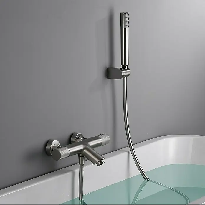 Imex Line Grifo termostático de bañera - Níquel - Primer plano de un moderno grifo de bañera de níquel cepillado con teleducha contra una pared gris.