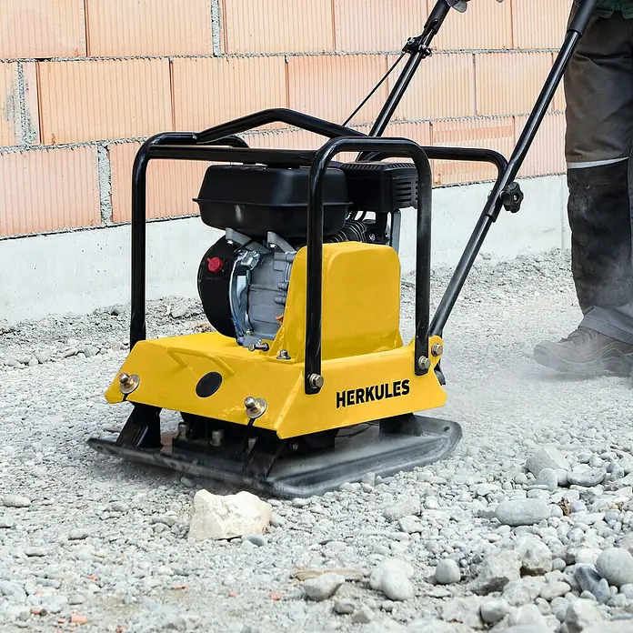 Herkules Rüttelplatte RP1800 - 4,8 kW, Verdichtungsdruck: 2.300 kg - Bild einer gelben Herkules-Rüttelplatte bei der Arbeit. Das Gerät verdichtet den Untergrund mit einem Bediener im Hintergrund.