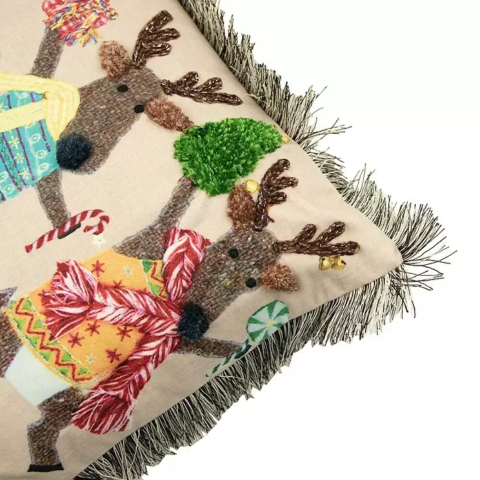 Kissen Rentiere - Weihnachten, 50 x 30 cm, 100 % Polyester - Nahaufnahme eines festlichen beigen Zierkissens mit gestickten Rentieren in bunten Pullovern und Schals, strukturierten Details, Pompons, Perlen und Fransenrand.
