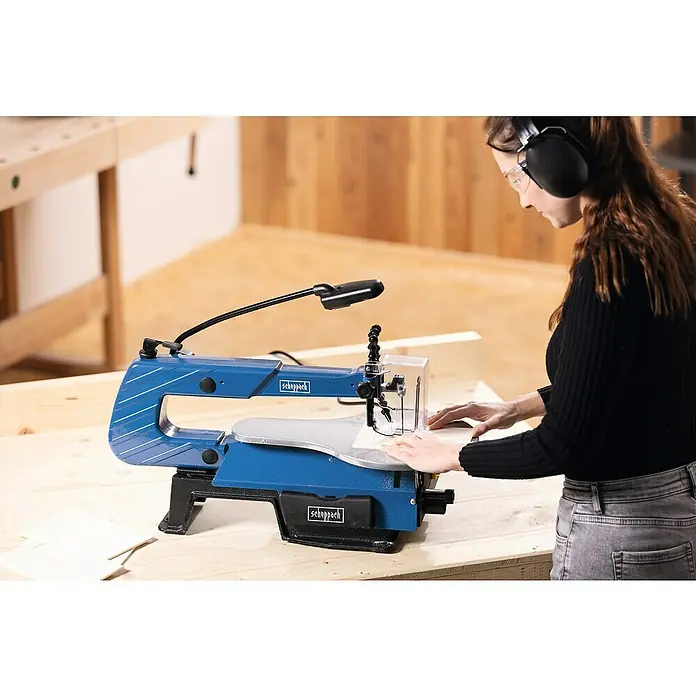 Scheppach Dekupiersäge SD 1600 V - 120 W - Nahaufnahme einer Scheppach Dekupiersäge in Aktion, mit einer Frau, die sie mit Schutzbrille und Kopfhörern bedient.