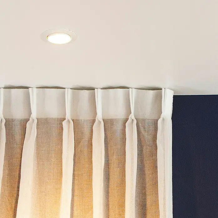 Innr Lighting Smart-LED-Lampe Spot Colour - GU10, Dimmbar, RGBW, 400 lm, 4,8 W, 2 Stk. - Vorhang aus hellem Stoff mit gerafftem Bund unter einer Deckenleuchte, der sanftes Licht verbreitet. Die Textur des Vorhangs sorgt für eine warme Atmosphäre.