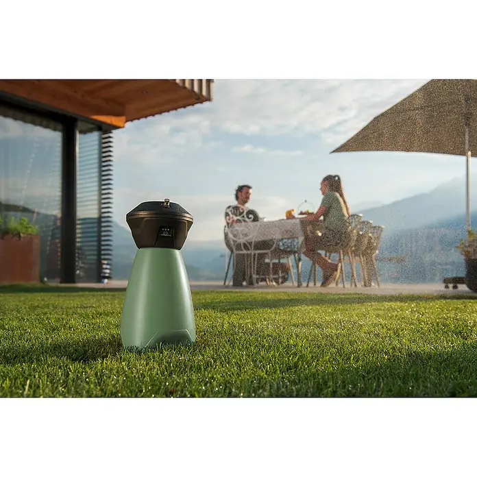 Stocker Geyser Stechmückenschutz Nebulisator - 2 l, 1 Akku - Rasensprenger-Roboter beim Bewässern eines grünen Rasens. Im Hintergrund sitzen zwei Personen an einem Tisch.