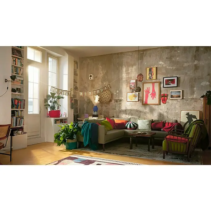 Tesa Powerstrips Selbstklebehaken - Eckig, Größe: S, Weiß, 3 Stk., Metall/Kunststoff - Ein gemütliches Wohnzimmer mit einer grauen Couch, bunten Kissen und einer Geburtstagsgirlande an der Wand. Die Wand hat einen dekorativen Putz.