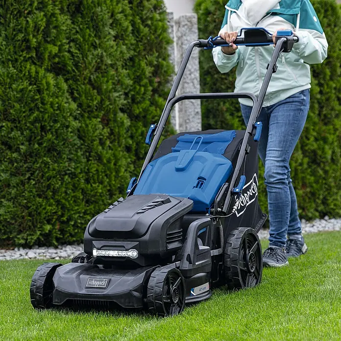 Scheppach IXES 20V Akku-Rasenmäher BC-MP470-X Set - 40 V, 4 Akkus, 4 Ah, Schnittbreite: 470 mm - Eine Person benutzt einen schwarzen und blauen Scheppach Rasenmäher, um den Rasen zu mähen.