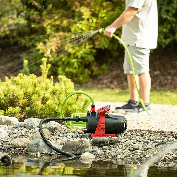 Scheppach Gartenpumpe GP600S - 600 W, Max. Fördermenge: 3.000 l/h - Rote und schwarze Wasserpumpe entnimmt Wasser aus einem Teich zur Gartenbewässerung.