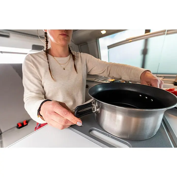 Petromax Kochgeschirr-Set Dimego - Edelstahl - Eine Person bereitet mit einem Topf auf einem Kochfeld in einem Wohnmobil eine Mahlzeit zu. Der silberne Topf steht im Mittelpunkt.