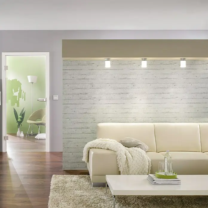 Diamond Doors Glasdrehtür Clear - 834 x 1.972 mm, Klarglas, Einscheibensicherheitsglas (ESG) - Ein elegantes Wohnzimmer mit einer hellen Couch, einem weißen Tisch und modernen Leuchten, die eine stilvolle Atmosphäre schaffen.