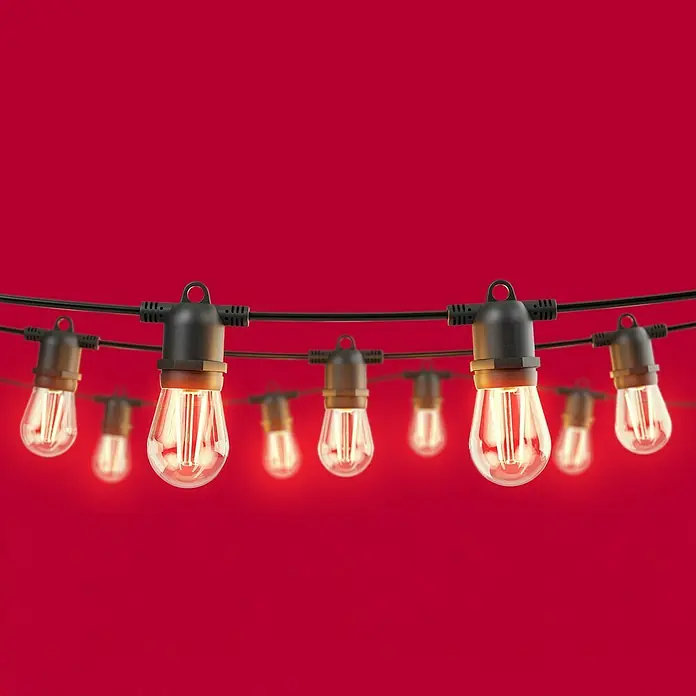 Innr Lighting Smart-LED-Lichterkette Verlängerung - Außen, 4 m, Lichtfarbe: Warmweiß, Anzahl Leuchtmittel: 8 Stk. - Eine Lichterkette mit Glühbirnen vor einem roten Hintergrund. Perfekt für stimmungsvolle Beleuchtung im Garten oder auf der Terrasse.