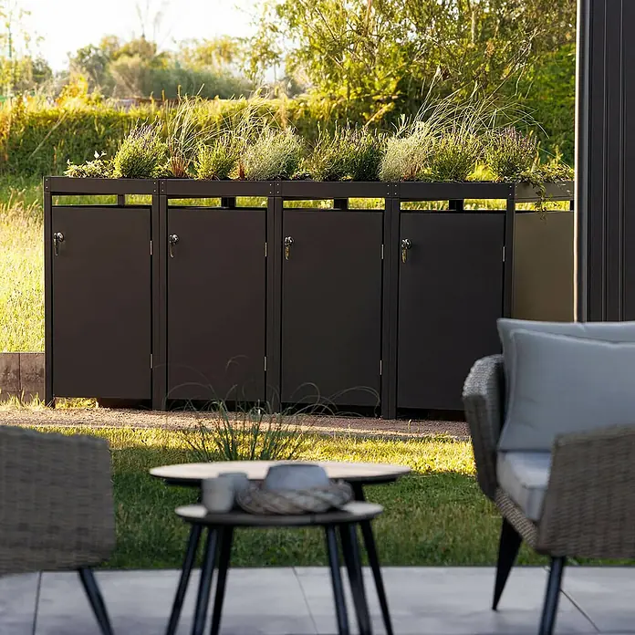 Metzler Mülltonnenbox - Stahl, Anthrazit, Geeignet für Anzahl Mülltonnen: 4 Stk., Mit Pflanzdach - Das Bild zeigt eine stilvolle Mülltonnenbox mit Pflanzkasten auf einer Terrasse. Die Box ist aus dunklem Metall gefertigt und bietet Platz für mehrere Tonnen.