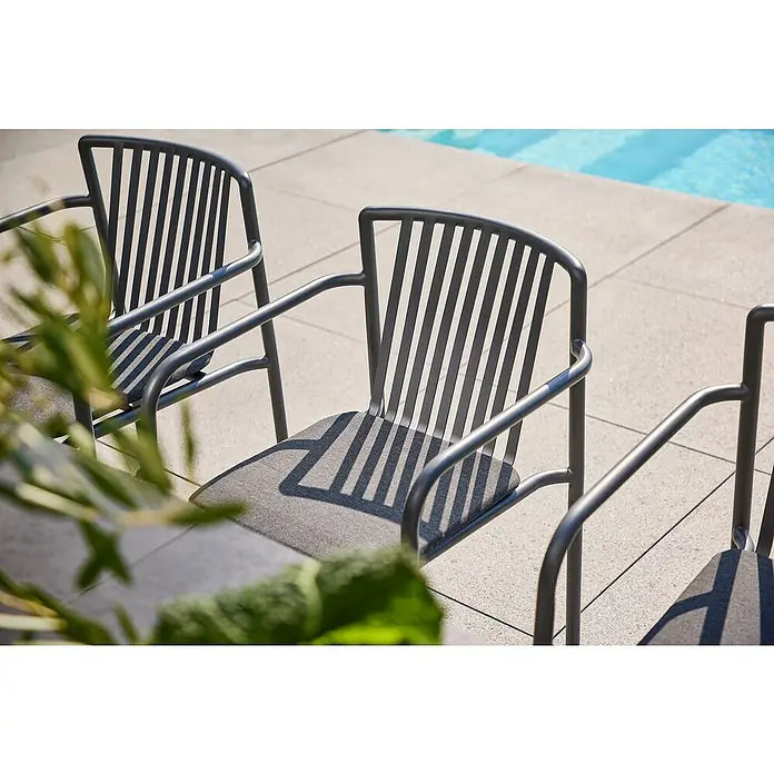 Sunfun Sarah Stapelsessel - Stapelbar, Night-Grey, B x T x H: 59 x 80 x 57 cm - Nahaufnahme von modernen grauen Gartenstühlen mit Armlehnen und Lattenmuster vor einem hellen Hintergrund und Pool im Freien.