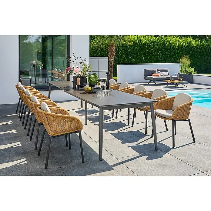 Sunfun Solo Garten-Tischplatte Erweiterung - L x B: 60 x 100 cm, Aluminium, Sintered Stone, Night-Grey - Ein grauer Gartentisch mit geflochtenen Armlehnstühlen auf einer Terrasse. Das Arrangement bietet stilvollen Komfort im Freien.