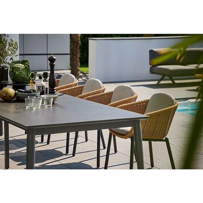 Sunfun Solo Gartentisch - L x B x H: 230 x 100 x 76,5 cm, Aluminium, Sintered Stone, Night-Grey, Ausziehbar - Outdoor-Szene mit einem grauen Esstisch und vier Rattanstühlen mit hellen Polstern auf einer Terrasse.