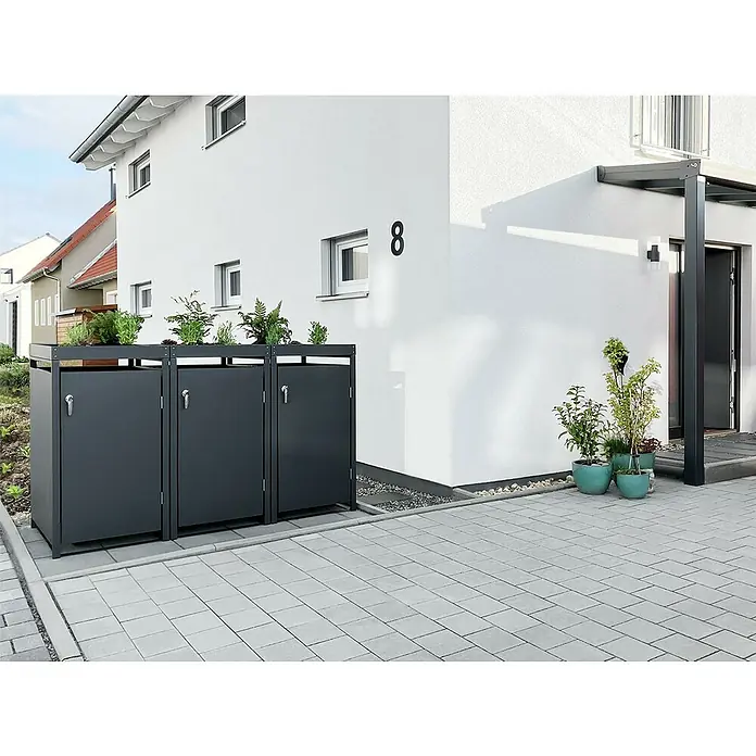 Metzler Mülltonnenbox - 198,5 x 80 cm, Stahl, Anthrazit, Geeignet für Anzahl Mülltonnen: 3 Stk., Mit Pflanzdach - Drei graue Mülltonnenboxen mit Pflanzen auf einem gepflasterten Hof vor einem weißen Haus.